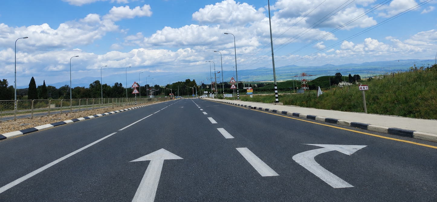 צילום כביש עם חיצי כיוון לבנים על האספלט ונוף פתוח באופק